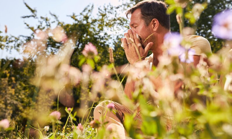 Mann in Gartenkulisse schnieft in ein Taschentuch | © Adobe Stock/ Robert Kneschke