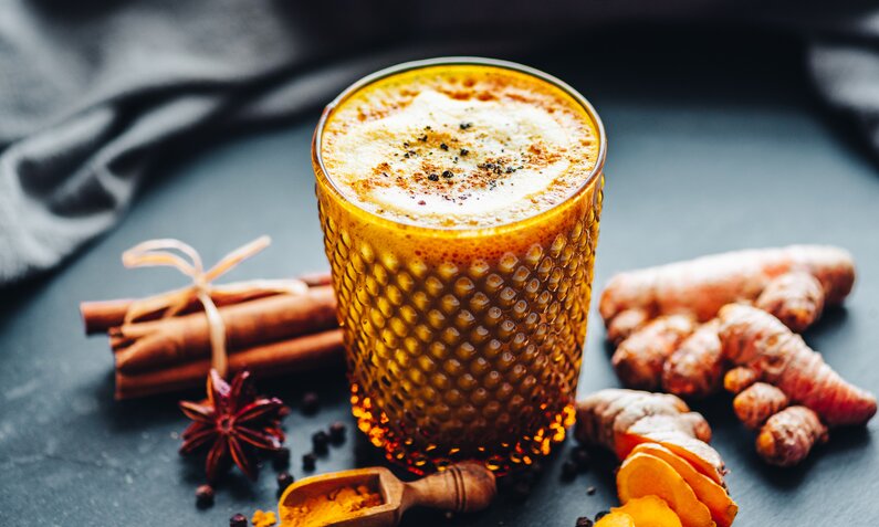 Glas gefüllt mit gelber Milch, bestreut mit Gewürzen, daneben Sternanis, Kurkumawurzel und Zimtstange. | © Getty Images / 	Rocky89