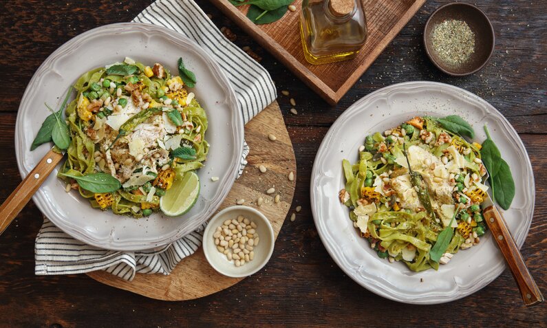 Auf zwei Tellern angerichtet Penne mit Hähnchen, Pinienkernen und grünem Basilikum-Pesto. | © Getty Images / luchezar