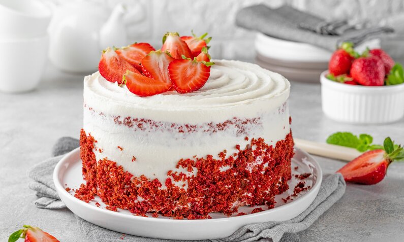Erdbeer-Sahne-Torte mit frischen Erdbeeren belegt auf weißem Tortenboden serviert. | © Adobe Stock / irina2511
