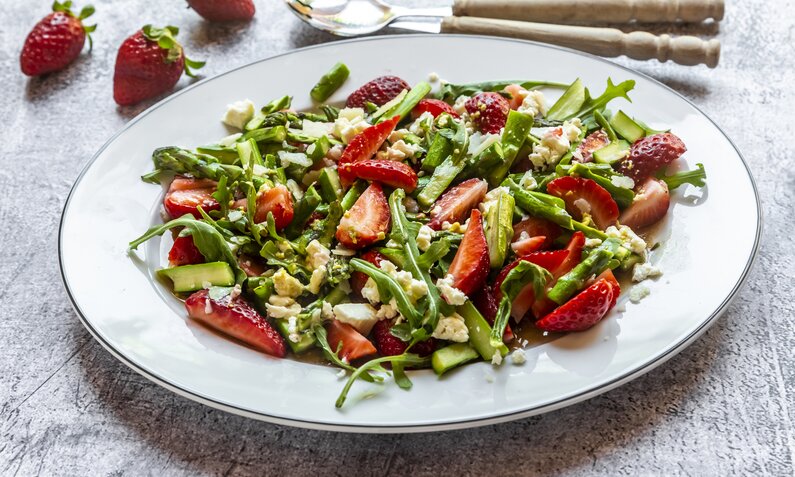 Erdbeer-Salat mit Feta und grünem Spargel, angerichtet auf weißem Teller. | © Getty Images /lacaosa