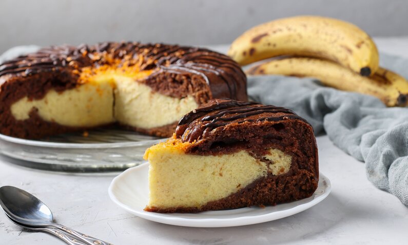 Angeschnittener Schoko-Bananenkuchen mit Quarkfüllung angerichtet auf einem Tortenboden. | © Getty Images /Angelika Mostova