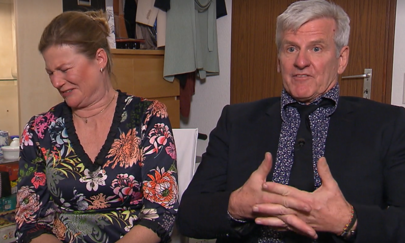 Ein älterer Mann im schwarzen Anzug erklärt etwas mit ernstem Gesichtsausdruck, während eine Frau neben ihm verlegen wegschaut. | © Screenshot Vox/RTL+