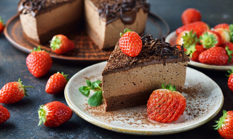 Angeschnittener Brownie-Käsekuchen auf Teller, Stück davon und frische Erdbeeren daneben. | © Getty Images / olvas