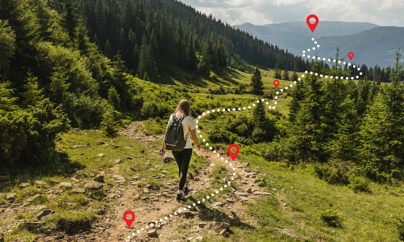 Junge Frau in hellem Shirt und dunkler Hose mit Rucksack von hinten, wie sie in einer grünen, waldigen Berglandschaft wandert, vor ihr eingezeichnet weiße gestrichelte kurvige Linie mit  | © Shi/ Adobe Stock