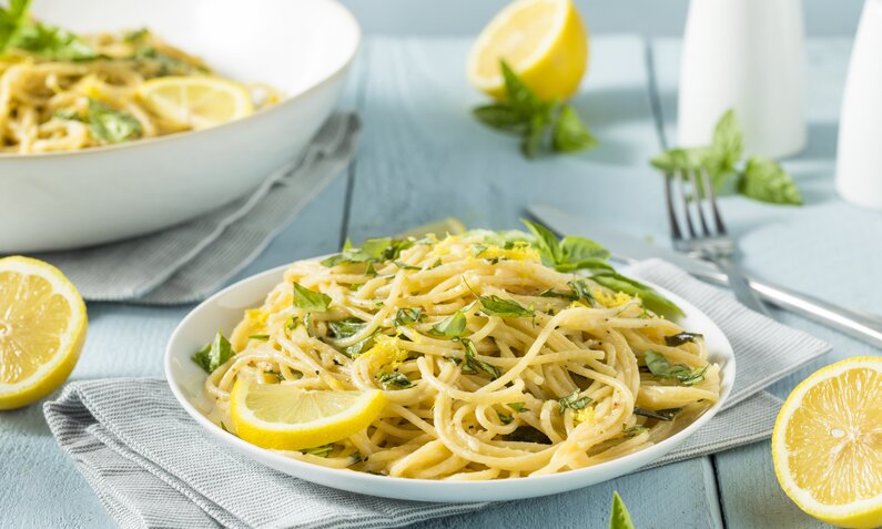 Pasta mit Zitrone und frischem Basilikum angerichtet in einem tiefen Pasta-Teller, daneben frische Zitronen. | © Getty Images / 	bhofack2