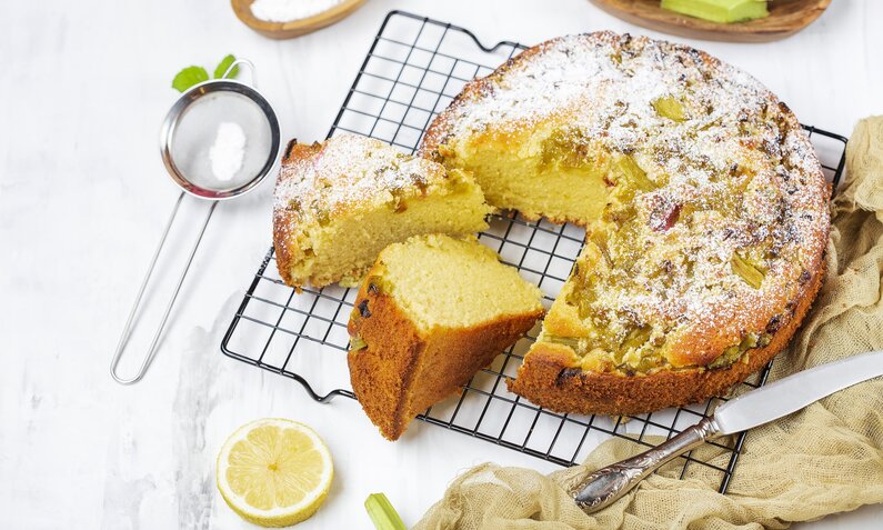 Angeschnittener Joghurtkuchen auf Küchengitter, daneben Zitronenscheiben. | © Getty Images /Pronina Marina