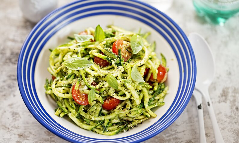 Zucchini-Salat in Pesto mit Cherry-Tomaten angerichtet auf blau-weißem Teller. | © Getty Images / 	Bartosz Luczak