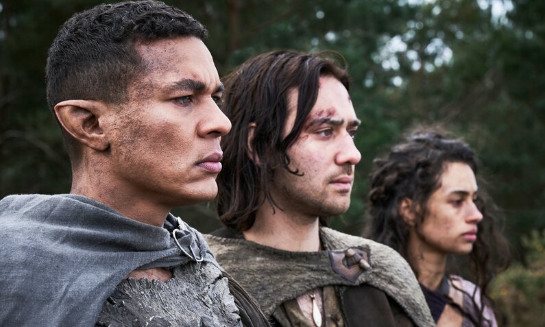 Ismael Cruz Córdova als Arondir , Max Baldry als Isildur und ein weiblicher Co-Star stehen Seite an Seite und blicken entschlossen in einer Szene aus "Der Herr der Ringe: Die Ringe der Macht" - Staffel 2 | © Amazon MGM Studios/ Prime Video