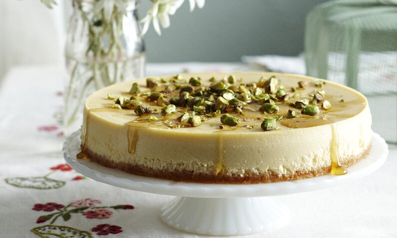 Joghurt-Torte ohne Zucker ohne Mehl angerichtet auf einer Tortenplatte dahinter Blumenstrauß. | © Getty Images / BRETT STEVENS