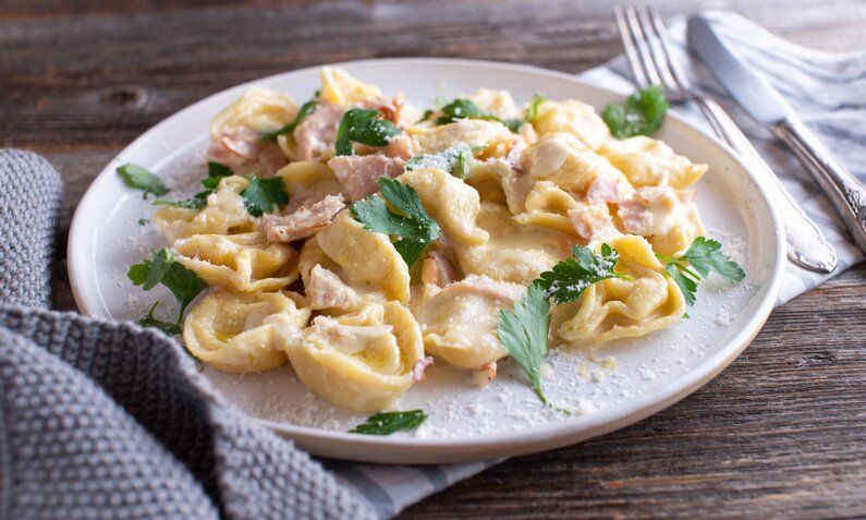 Tortelloni in Sahnesoße mit Schinken auf einem weißen Teller angerichtet. | © Getty Images / Angelika Heine