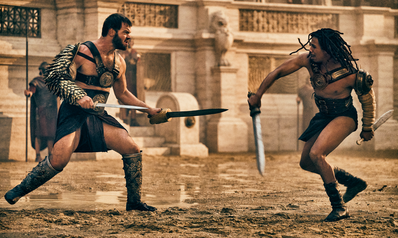 Zwei kampfbereite Gladiatoren stehen sich in der Arena gegenüber in einer Szene aus der Serie "Those About To Die" | © 2024 Peacock TV LLC, All Rights Reserved/Amazon Prime Video