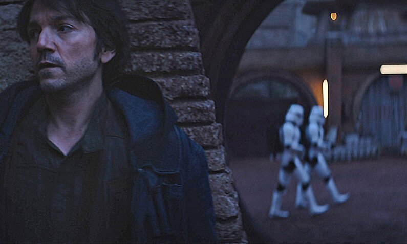 Diego Luna lehnt bei Nacht draußen an einer Mauer in einer Szene aus der "Star Wars"-Serie "Andor" - im Hintergrund sind zwei Startrooper zu sehen | © Lucasfilm Ltd./Disney+