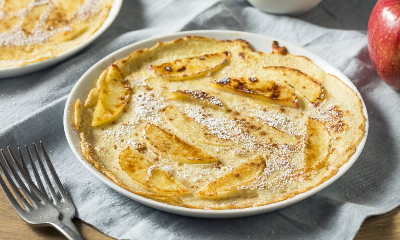 Apfelpfannkuchen auf weißem Teller liegend, daneben weitere Apfelpfannkuchen auf Teller. | © Getty Images / bhofack2