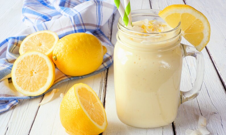 Zitronen-Joghurt-Smoothie im Glas, darin ein Strohhalm und daneben frische Zitronen. | © Getty Images / jenifoto