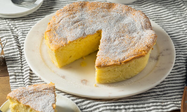 Angeschnittener Quarkkuchen auf einem weißen Kuchenteller auf einem Holztisch. | © Getty Images / 	bhofack2