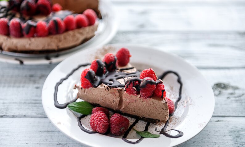 Angeschnittener Schokomousse-Kuchen mit frischen Himbeeren auf einem weißen Dessertteller. | © Getty Images / 	lisegagne