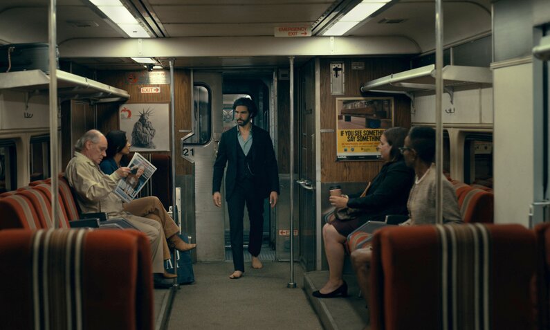 Tahar Rahim steht  in einer Szene aus dem Kinofilm "Madame Web" mit dem Rücken zur Wand in einem düsteren Ubahn-Waggon, in dem einige Leute sitzen. | © Imago Images/Picturelux