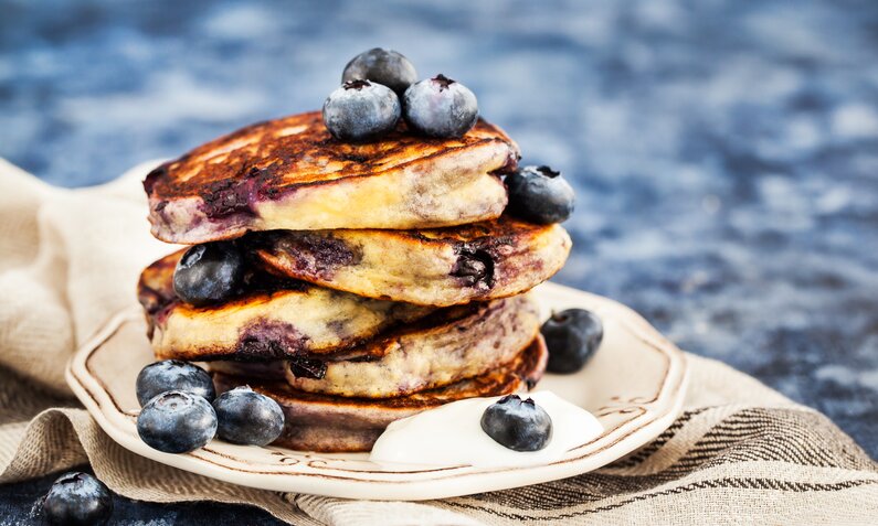 Fluffige Blaubeer-Pfannkuchen gestapelt auf einem Teller, der auf einem Leinentuch steht. | © Adobe Stock / kate_smirnova