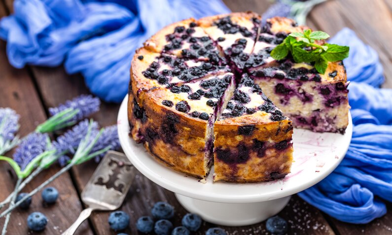 Angeschnittener Joghurtkuchen mit Blaubeeren daneben frischer Lavendel. | © Getty Images / YelenaYemchuk