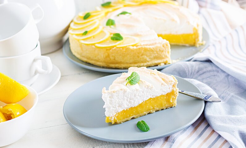 Angeschnittener Quarkkuchen mit Zitronenmousse, dekoriert mit frischen Zitronenscheiben. | © Adobe Stock / timolina