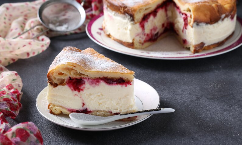 Stück Kirsch-Joghurtkuchen im Vordergrund dahinter angeschnittener Kuchen. | © Adobe Stock / Anzhela