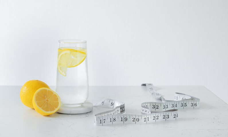 Ein Glas Wasser mit Zitrone, daneben ein Maßband | © Adobe Stock/ Svetlana