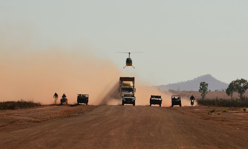 Aif einer staubigen Straße im Outback rasen ein LKW, Trucks, Motorräder und ein Hubschrauber auf den Betrachter zu in einer Szene aus der Netflix-Serie "Territory" | © Netflix