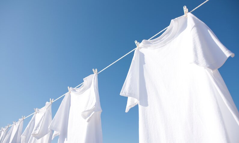 Weiße T-Shirts hängen an einer Wäscheleine vor klarem, blauem Himmel in der Sonne. | © Adobe Stock/ Paylessimages