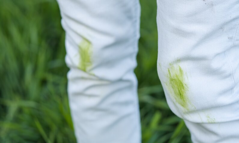 Weiße Jeans mit frischen Grasflecken an den Knien, im Hintergrund saftiges grünes Gras. | © Adobe Stock/ HalynaRom