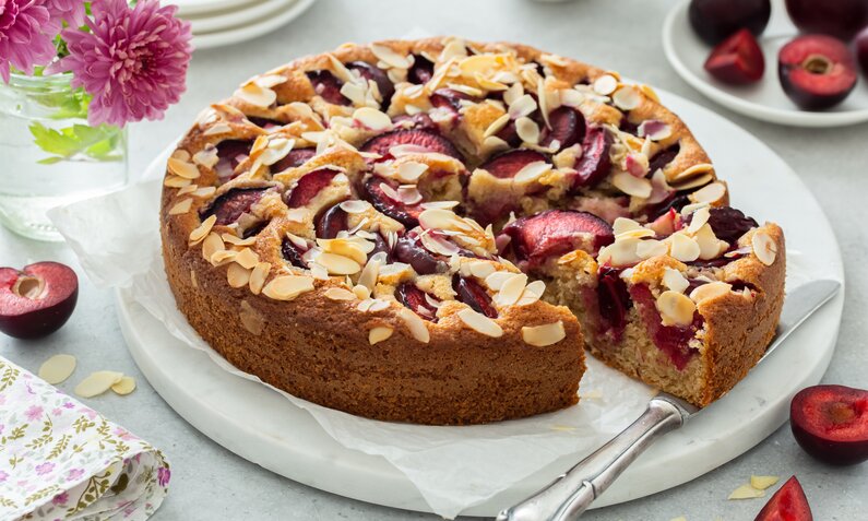 Angeschnittener Low Carb Pflaumenkuchen mit Mandelblättern garniert auf einem Kuchenteller. | © Getty Images / Anna_Shepulova