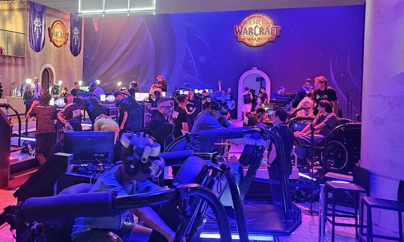 VR-Spieler vertieft in Simulationen, während Besucher in einer mit blauen Lichtern erleuchteten Halle den World of Warcraft-Stand erkunden. | © Sabrina Forst